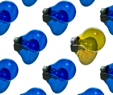 One yellow light bulb among many blue light bulbs on a white background.