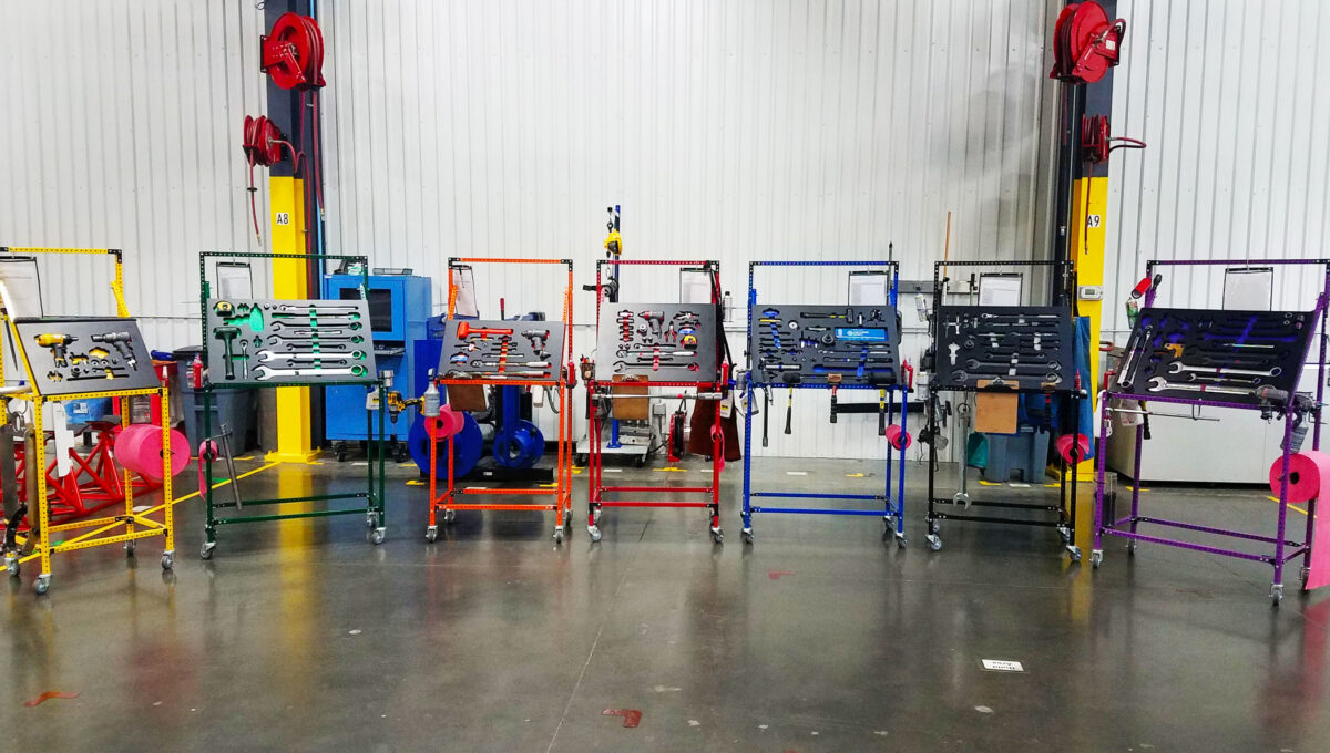Seven different colored (yellow, green, orange, red, blue, black, and purple) Flex Craft Shadow Box Tool Carts sitting side-by-side on the manufacturing production floor.