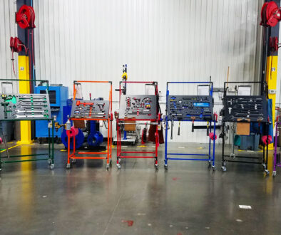 Seven different colored (yellow, green, orange, red, blue, black, and purple) Flex Craft Shadow Box Tool Carts sitting side-by-side on the manufacturing production floor.